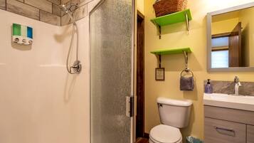 Un baño con ducha, inodoro y lavabo, con estantes verdes sobre el lavabo.