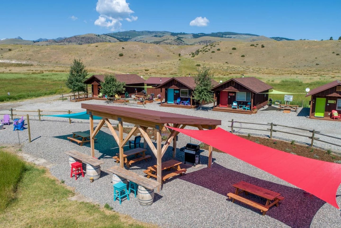 A campground with wooden cabins, picnic tables, and a playground area.