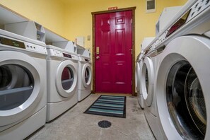 Un cuarto de lavandería con varias lavadoras, una puerta de salida roja y un tapete azul y blanco a rayas.