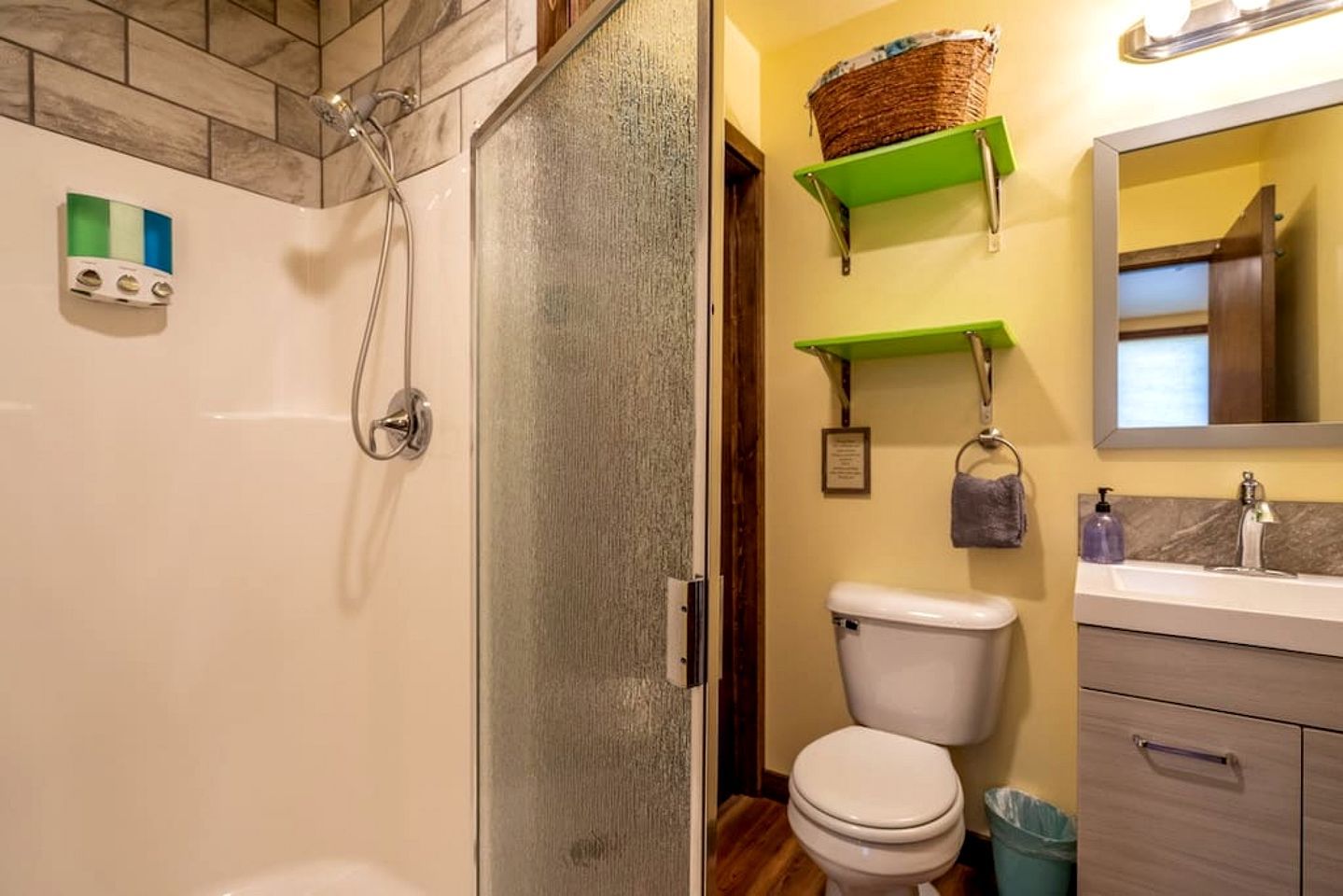 A bathroom with a shower, toilet, and sink, with green shelves above the sink.