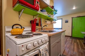 Una cocina compacta con una estufa blanca, un hervidor amarillo, una puerta verde y un lavabo.