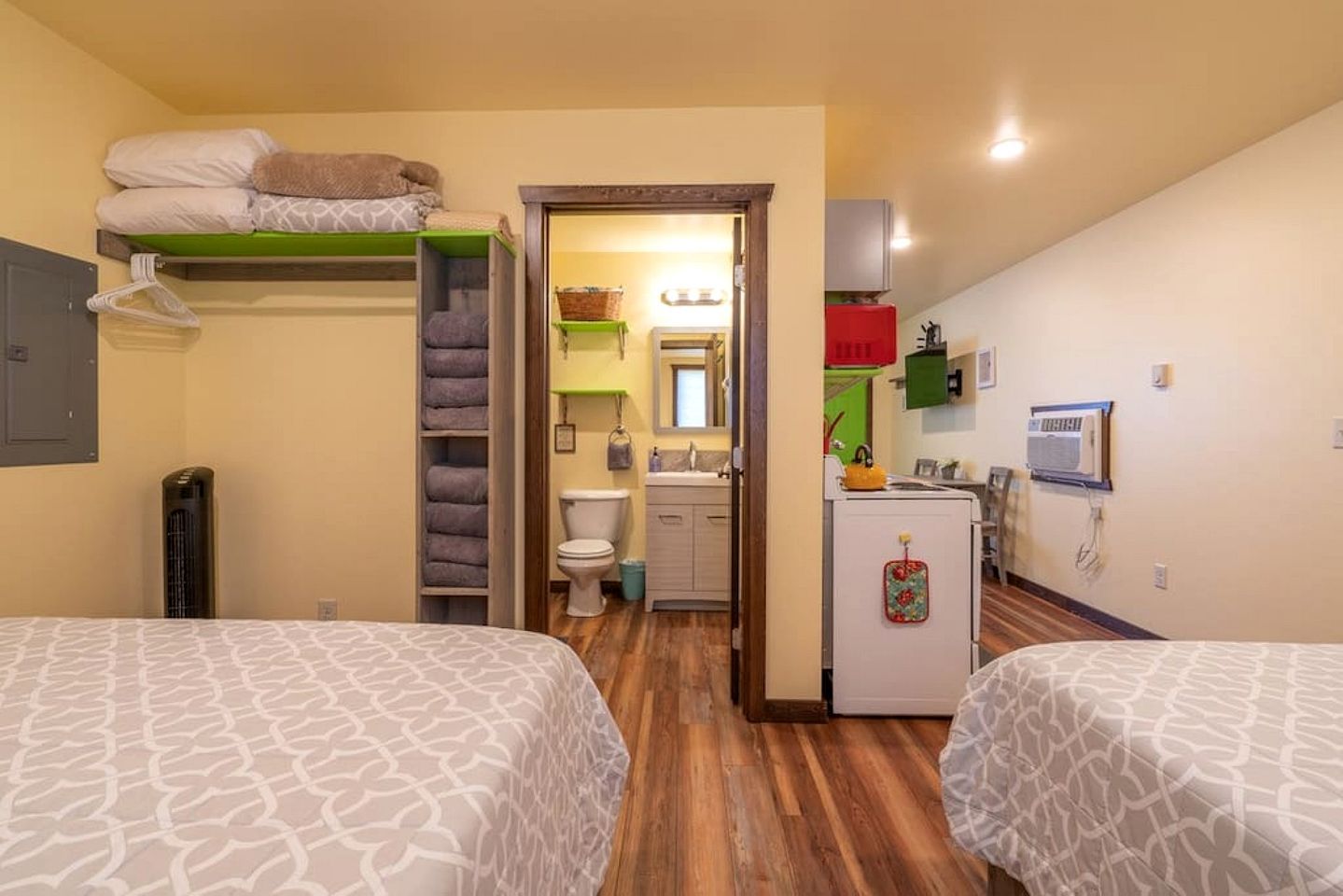 A compact hotel room with two beds, a kitchenette, a bathroom, and a small sitting area.
