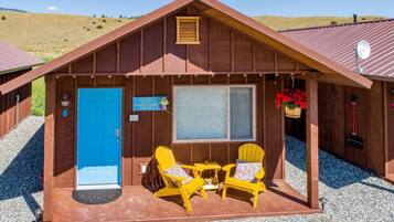 A cabin with a blue door, two yellow chairs, a small table, and a window.