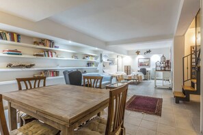 Un vaste espace de vie comprenant une table à manger en bois, plusieurs chaises, un canapé, une table basse et une bibliothèque remplie de livres.