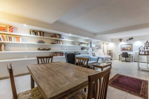 Ein großzügiger Wohnbereich mit Esstisch aus Holz, Stühlen, einer Couch und einem Bücherregal voller Bücher.
