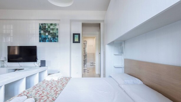 Quarto de hotel moderno com cama, televisão, escrivaninha e área de chuveiro.