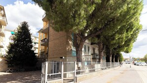 Um edifício residencial com entrada por portão, rua arborizada e bicicletas estacionadas.