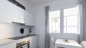 Cozinha compacta com armários brancos, forno embutido e janela com cortinas.