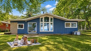 Une maison à l’extérieur bleu, dotée de grandes fenêtres et d’un porche abrité.