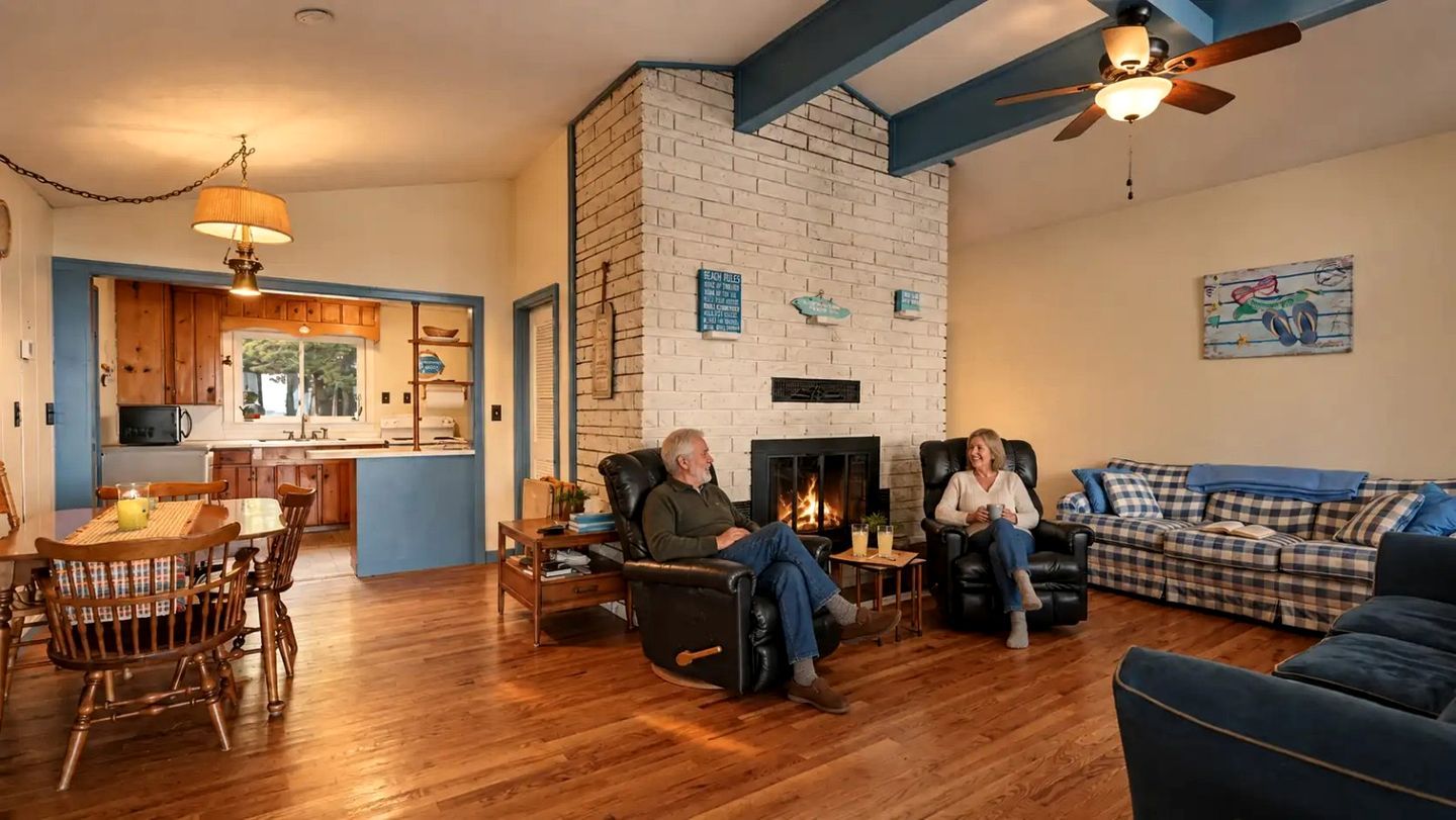 A living room with a fireplace, a dining area with wooden furniture, and a kitchen with blue walls.