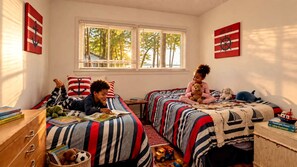 Una camera da letto con due letti, una finestra con persiane e diversi giocattoli e libri per bambini.