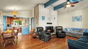 Una sala de estar con chimenea, un comedor con mesa y sillas de madera, y una cocina con armarios azules.