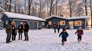 Ett tvåvåningshus med ett garage, omgivet av snötäckta träd.