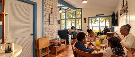 Un coin repas avec une table en bois, des chaises et une table basse. On y trouve un mur en briques et une fenêtre donnant sur un paysage agréable.