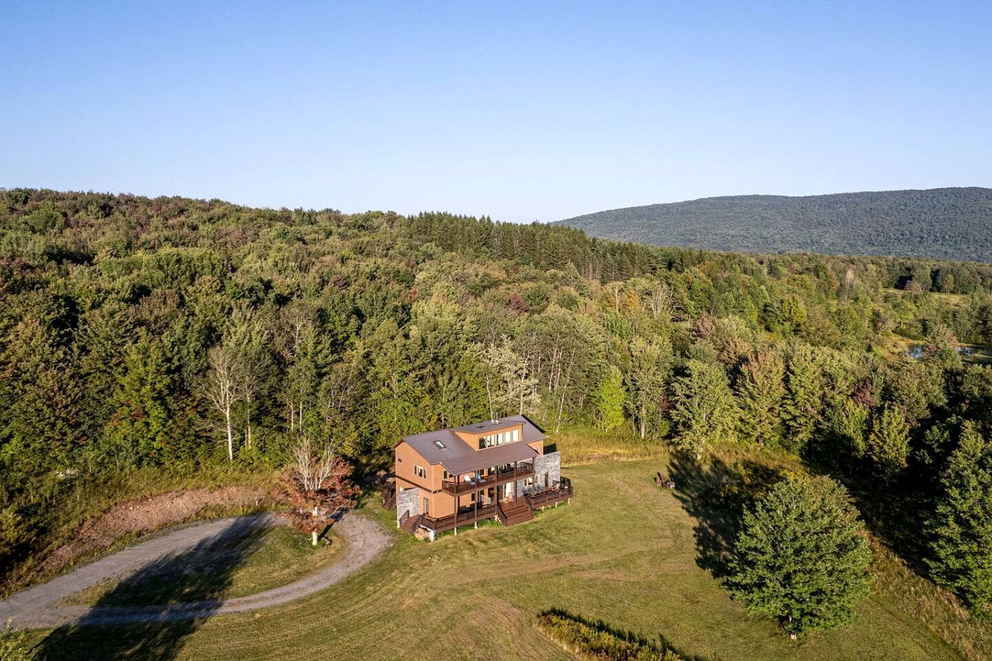 A two-story house with a stone foundation, surrounded by a forested area and a clear sky.