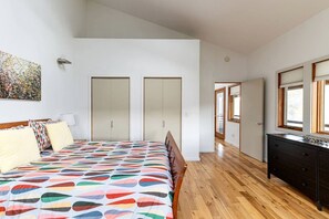 Ein Schlafzimmer mit Bett, Kommode, Kleiderschrank und einem Gang zu einem weiteren Raum.