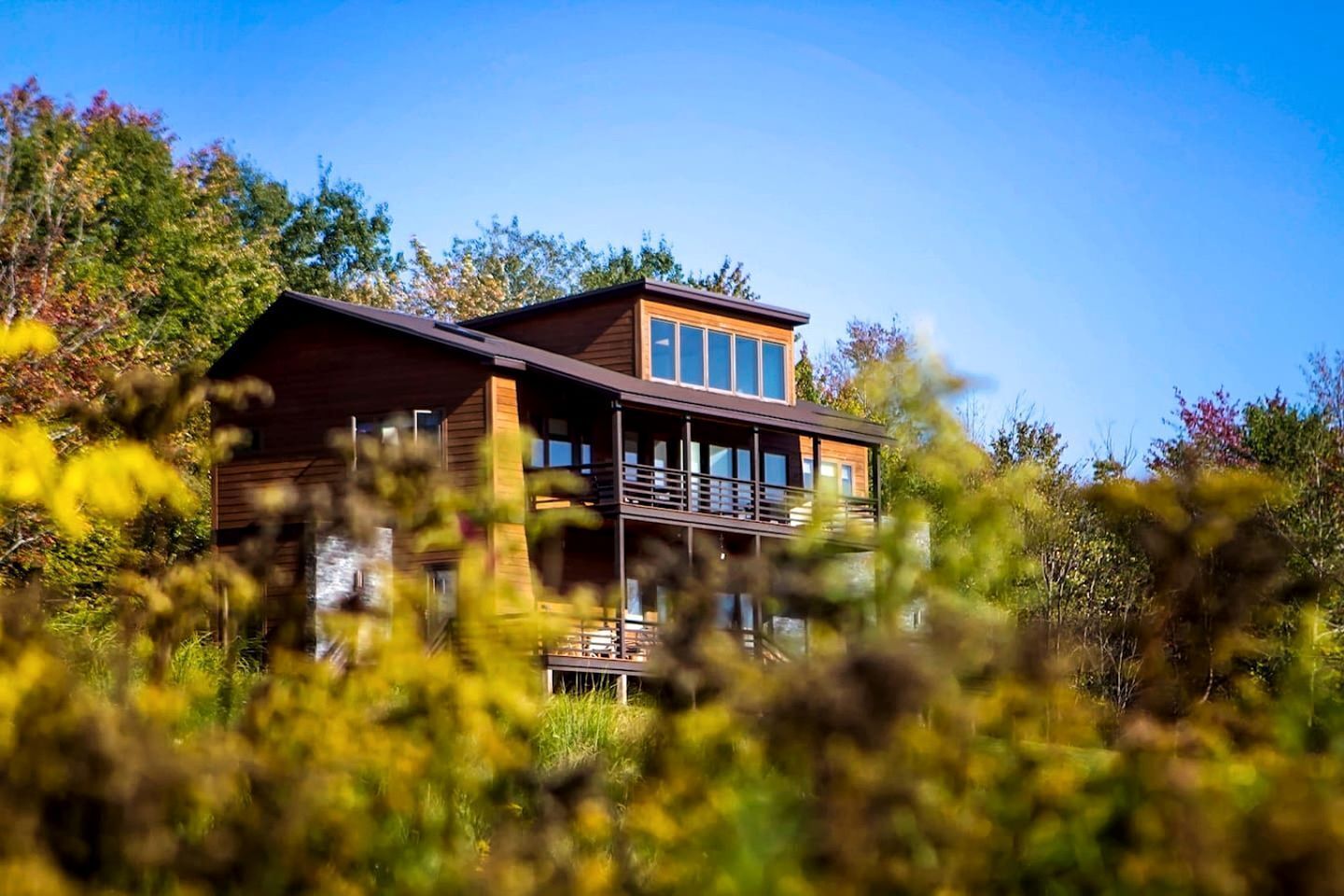 A two-story building with large windows and a balcony, surrounded by trees.