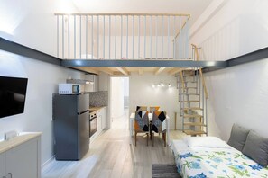 A compact apartment with a kitchenette, a dining area, a bed, and a staircase to an upper level. - Andreini (Bologna)