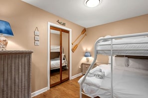 Une chambre avec un lit superposé, une porte en bois, une petite table de chevet avec une lampe et un panier en osier.