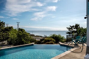 A swimming pool with a view of the sea, surrounded by greenery and a deck with chairs. - Gorgeous Beach House with Incredible Water Views for an Unforgettable Escape in Duck, North Carolina (Duck)