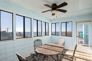 A sunroom with a table and chairs, large windows, a ceiling fan, and a view of the ocean. - Gorgeous Beach House with Incredible Water Views for an Unforgettable Escape in Duck, North Carolina (Duck)