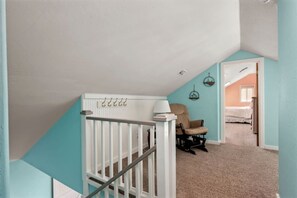 Un escalier avec une rampe blanche, une chaise et une lampe dans une pièce aux murs de couleur turquoise et au sol recouvert de moquette.