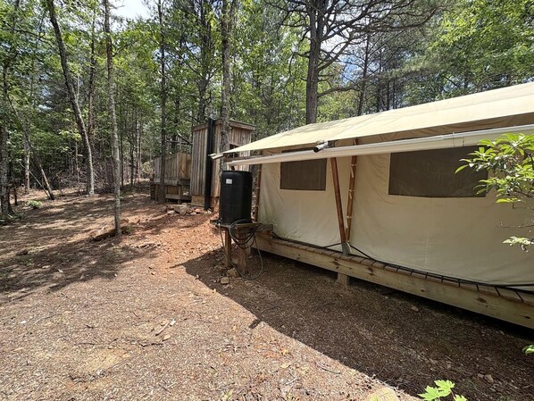 A forested campsite with a large tent and a black water tank.