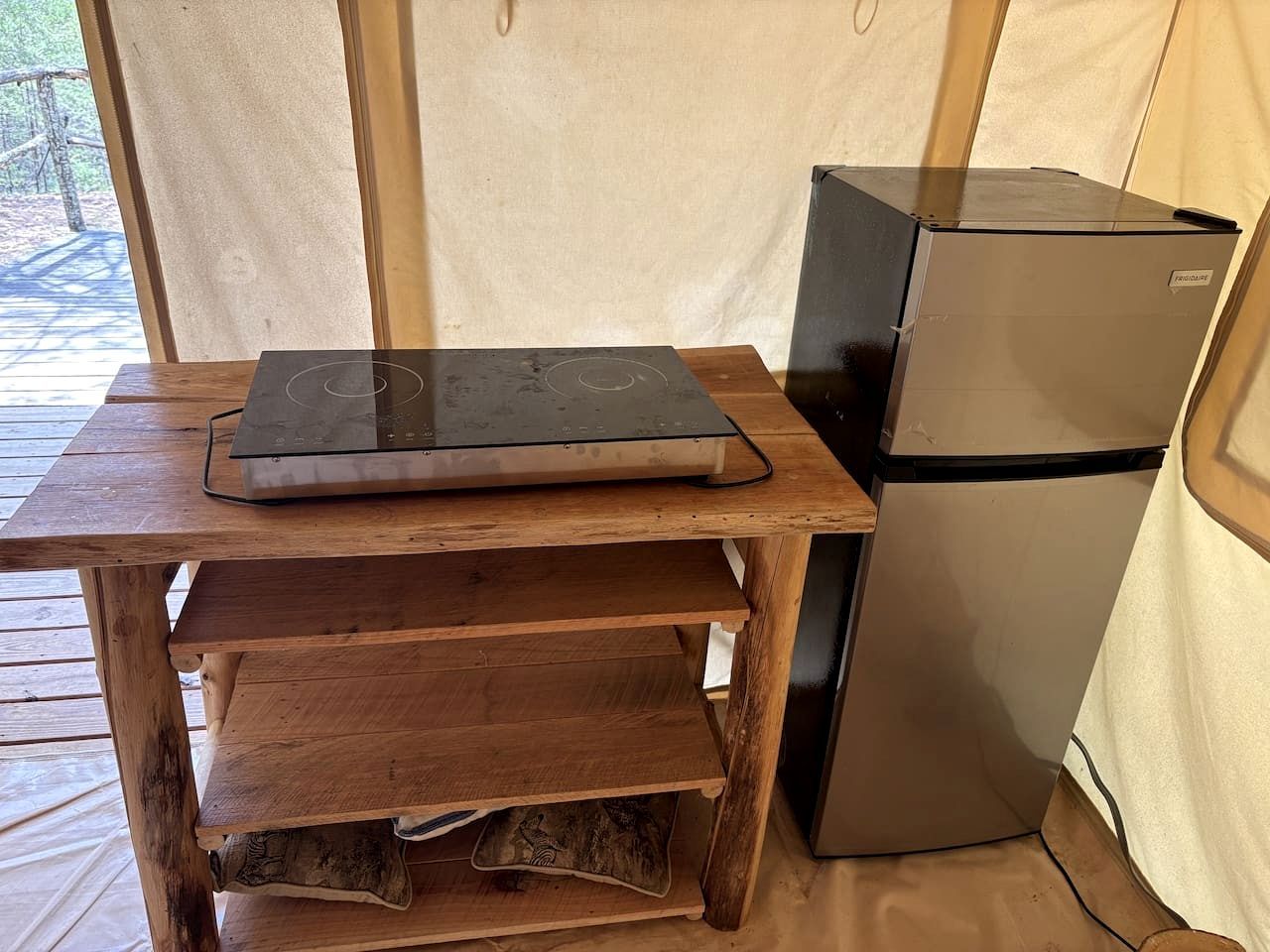 A wooden table with a laptop, a refrigerator, and a tented structure.
