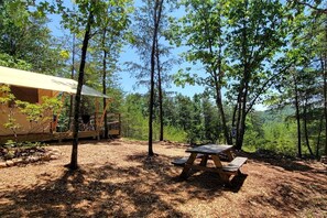 Un terrain de camping boisé, équipé d’une table de pique-nique et d’une tente.
