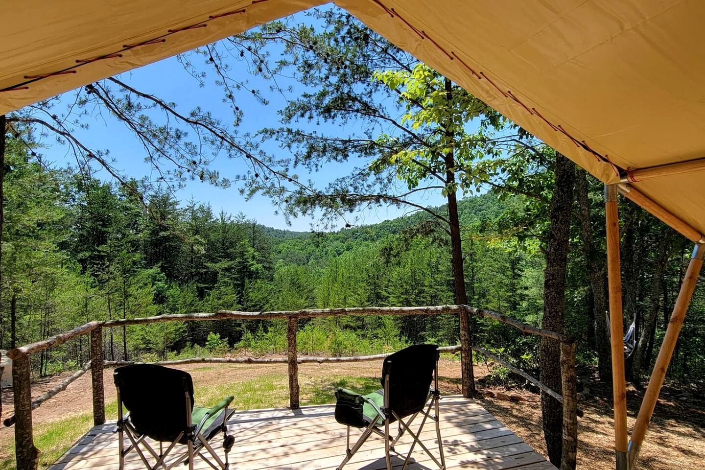 Un espacio al aire libre techado con dos sillas, rodeado de árboles y un paisaje boscoso.