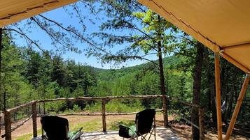 Un espacio al aire libre techado con dos sillas, rodeado de árboles y un paisaje boscoso.