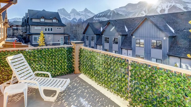 A balcony with a view of mountains, a row of houses, and a chair. - Warm Mountain View Retreat (Canmore)