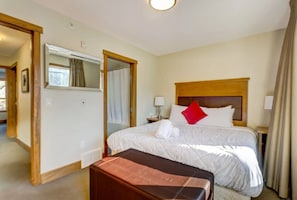 A hotel room with a large bed, a wooden headboard, a bedside table with a lamp, and a bathroom visible through an open door. - Warm Mountain View Retreat (Canmore)