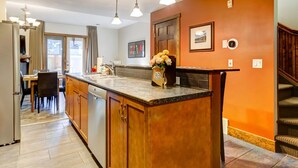 A kitchen with a central island, wooden cabinets, a dining area with a table and chairs, and a staircase leading to an upper level. - Warm Mountain View Retreat (Canmore)