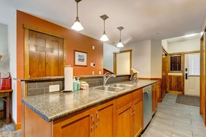 A kitchen with wooden cabinets, a granite countertop, a sink, and pendant lighting. - Warm Mountain View Retreat (Canmore)