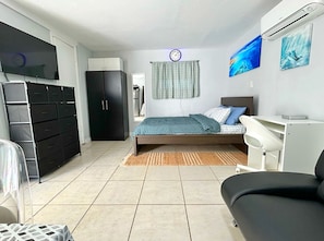Ein Schlafzimmer mit einem Bett, einem Kleiderschrank, einem Schreibtisch, einer Klimaanlage und einem Fernseher.