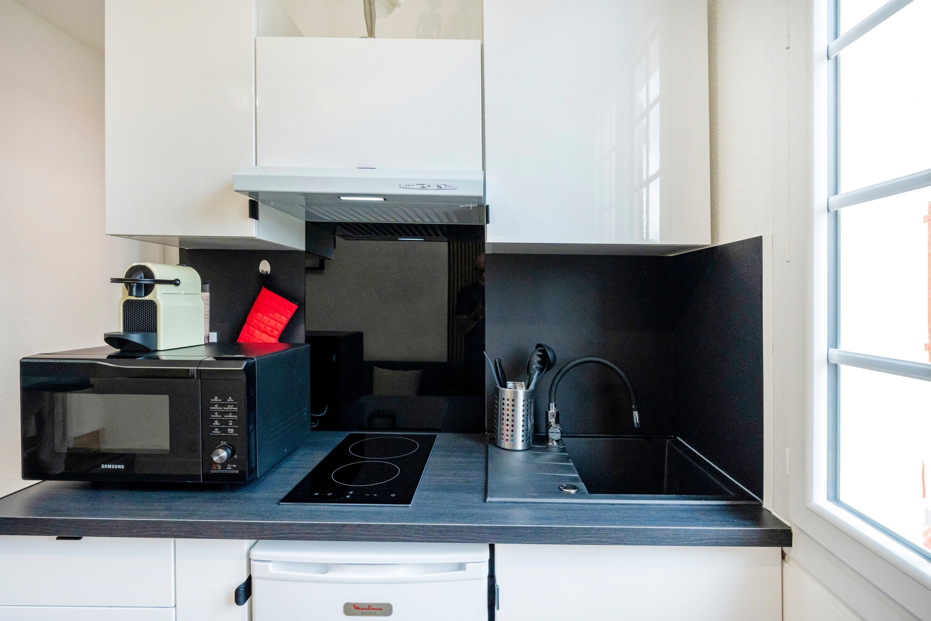 Una cucina compatta con forno a microonde, piano cottura, lavello e mobili bianchi.