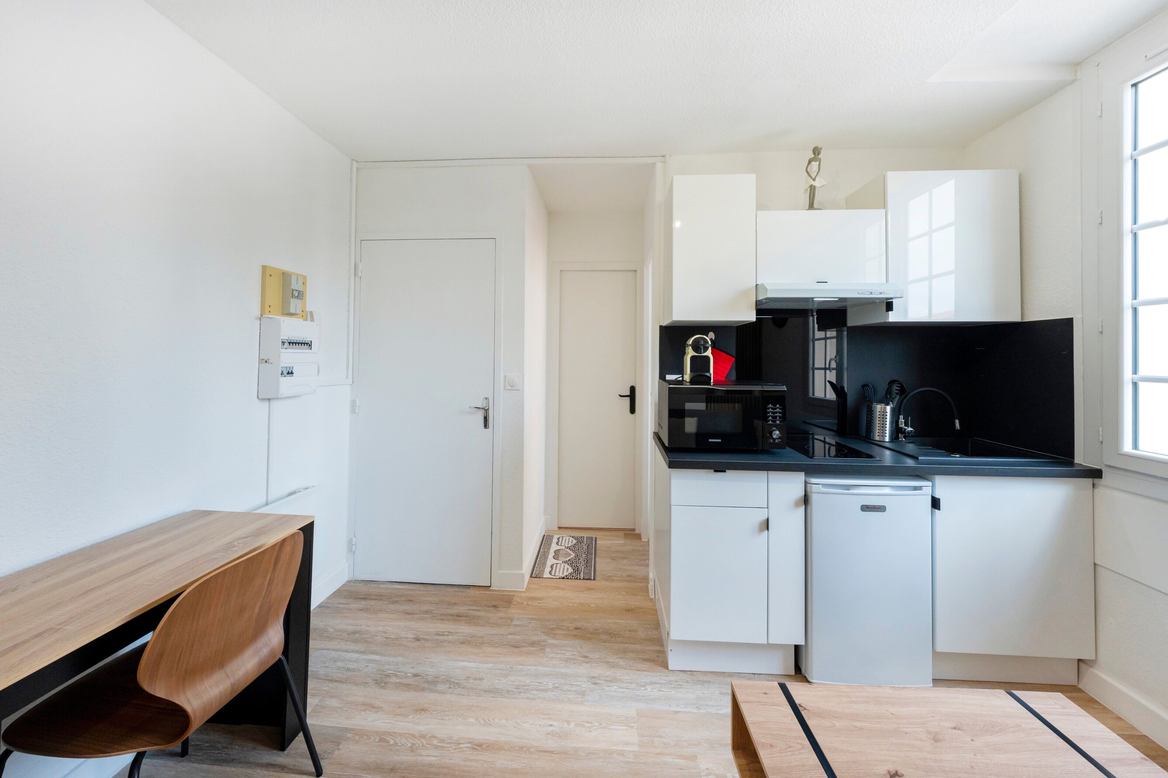 Een kleine keuken met witte kasten, een zwart aanrecht, een magnetron, een koffiezetapparaat en een vaatwasser.