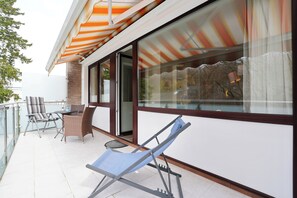 Ein Balkon mit Glastür, blauem Lounge-Stuhl und gestreiftem Sonnenschirm.