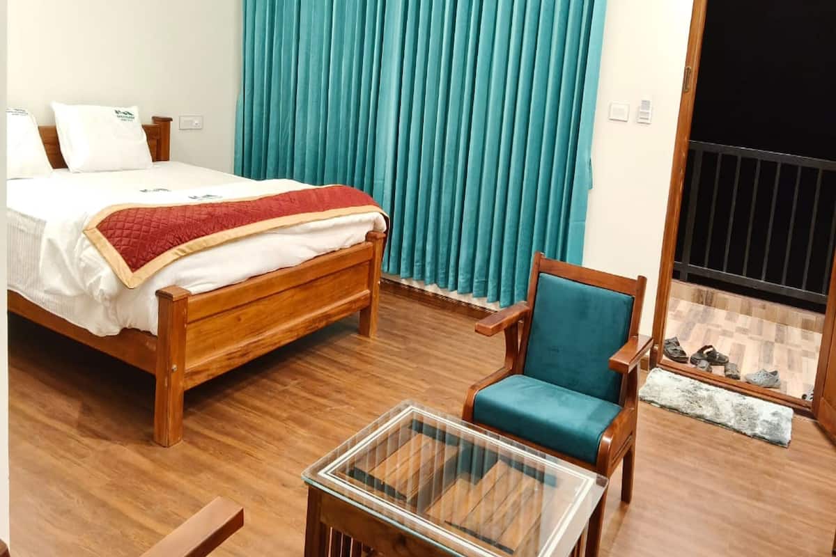 A bedroom with a wooden bed, a glass-top table, a blue chair, and a large window with teal curtains.