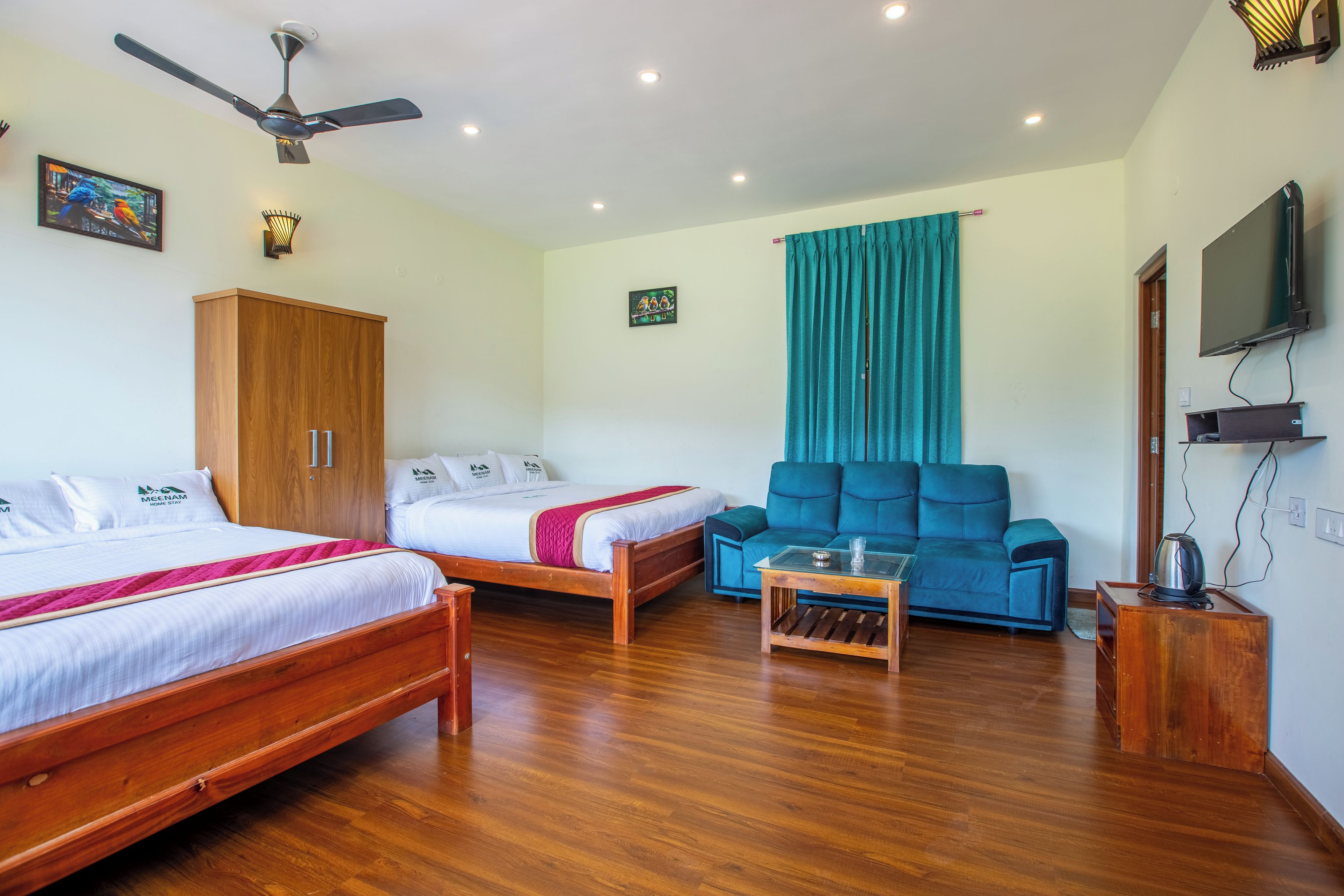 Una habitación de hotel con dos camas de madera, un sofá, un ventilador de techo y un televisor.