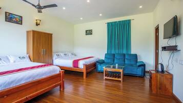Una habitación de hotel con dos camas de madera, un sofá, un ventilador de techo y un televisor.