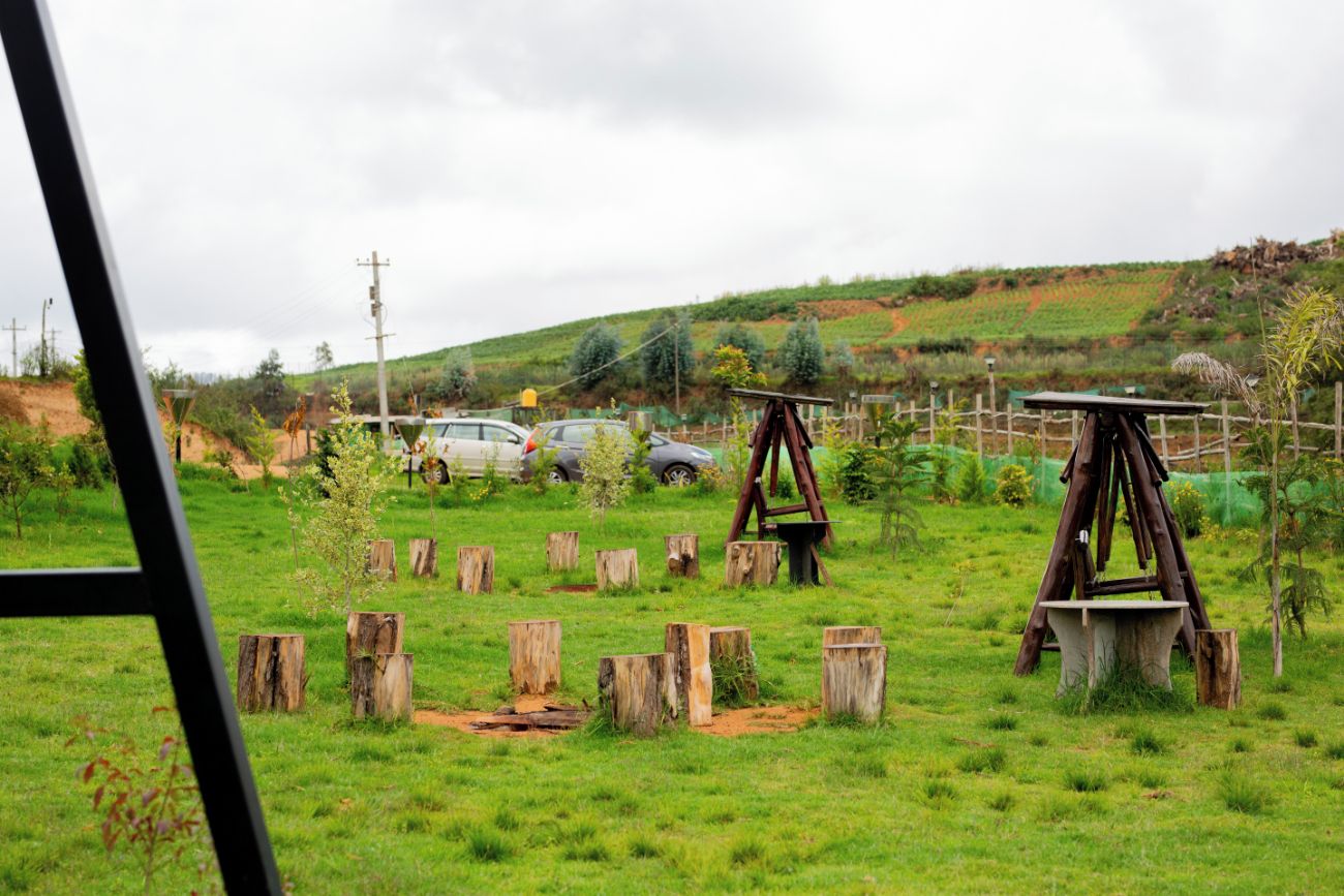 A grassy field with wooden structures, a fence, and parked cars.