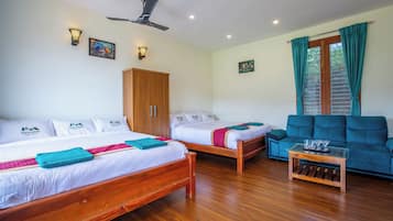 Une chambre d’hôtel avec deux lits en bois, un canapé bleu, une table basse en bois et un ventilateur de plafond.