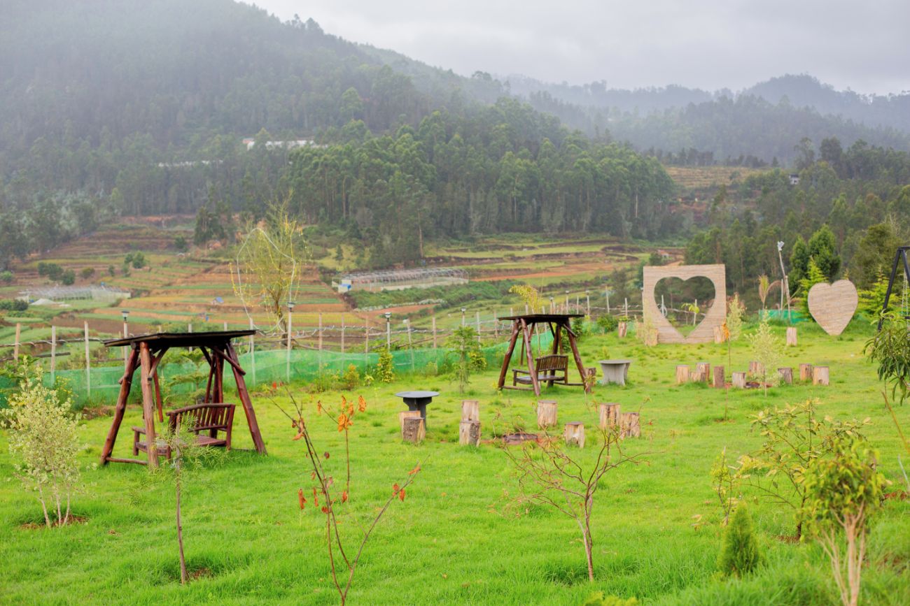 A rural landscape with a wooden swing set, a heart-shaped stone structure, and a fenced field.