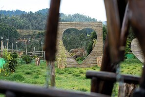 Una estructura con forma de corazón, superficie espejada, rodeada de una valla de bambú y follaje.