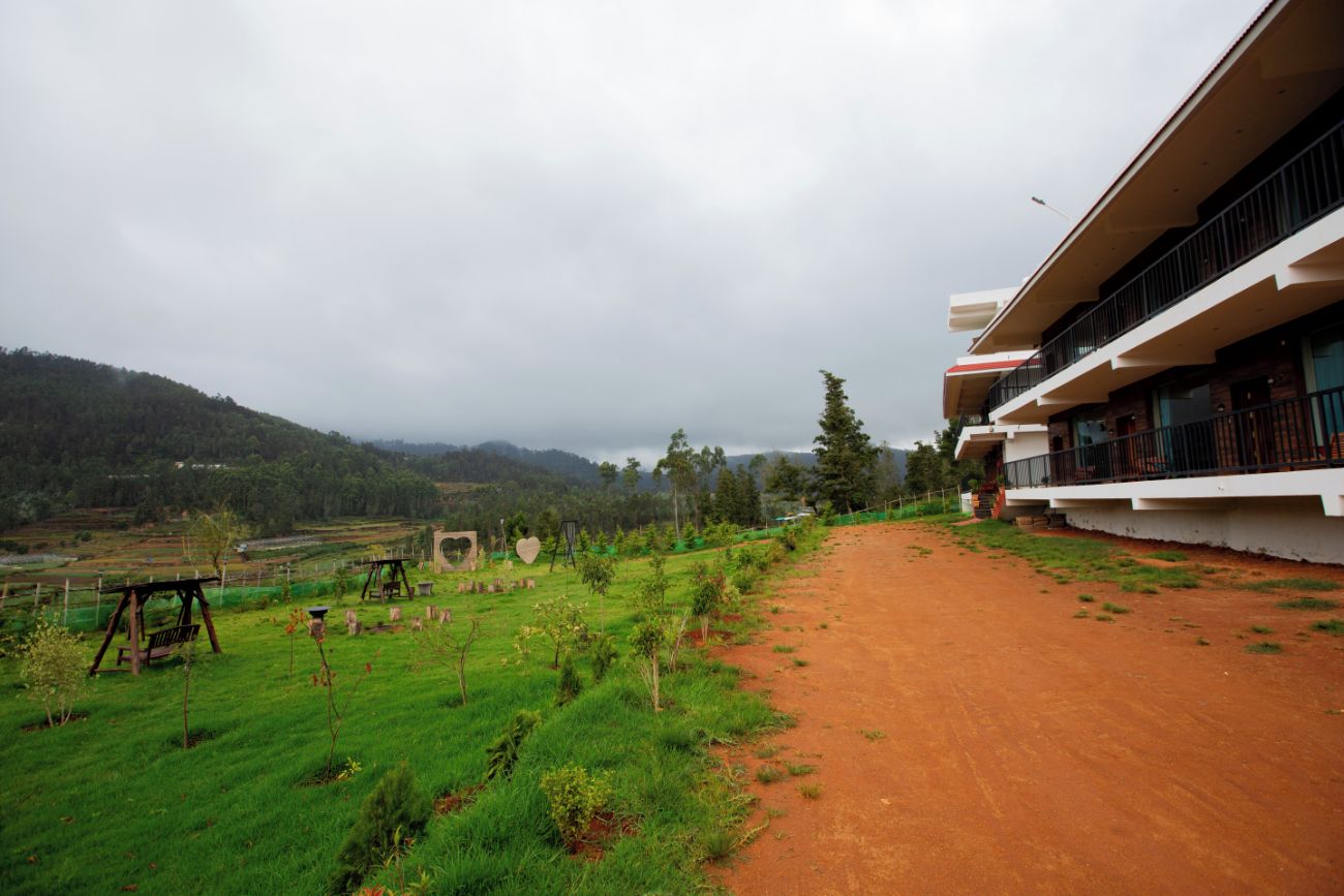 A building with a dirt path leading to a green field, surrounded by hills.