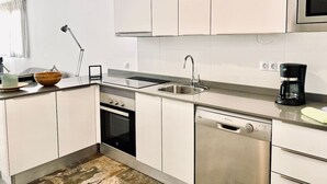 Ett modernt kök med vita skåp, vitvaror i rostfritt stål, en kaffebryggare och en skål på bänkskivan.
