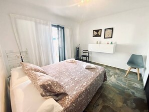 Ein Schlafzimmer mit einem Bett, einem Sessel, einem Schreibtisch und einem Regal mit Gegenständen.