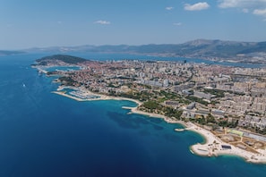 Vista aérea de una ciudad costera con un puerto deportivo, zonas residenciales y montañas al fondo.